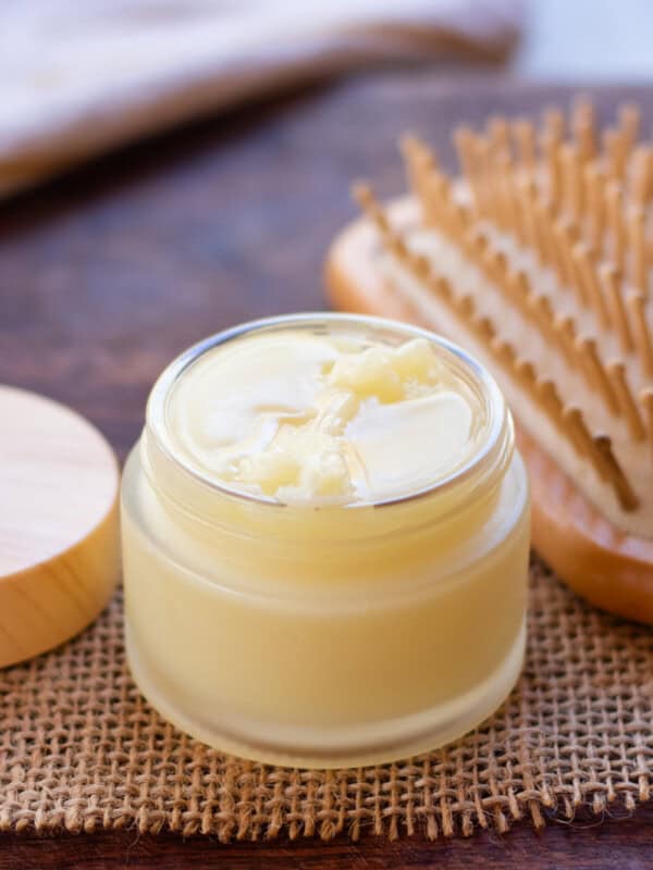 Small jar of DIY hair pomade with a wooden brush in the background.