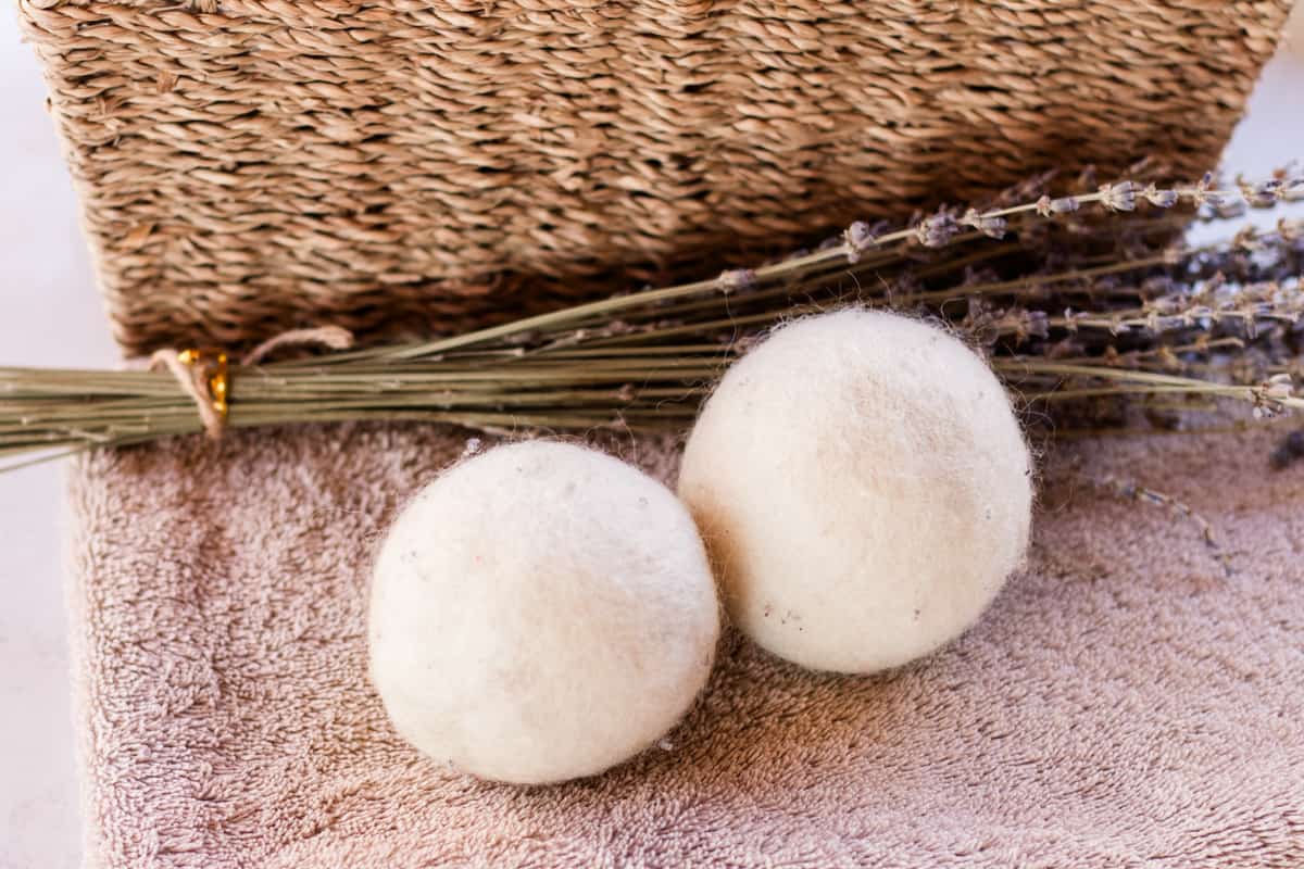 Two white dryer balls on a brown towel soaking up fragrance from a lavender sprig.