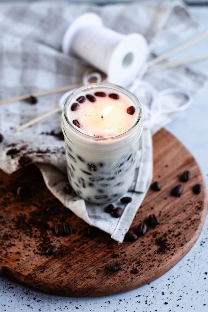 A lit homemade coffee candle in a small jar burning brightly.