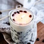 A DIY Coffee candle burning in a room with whole coffee beans spread around it.