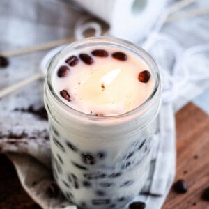 A DIY Coffee candle burning in a room with whole coffee beans spread around it.
