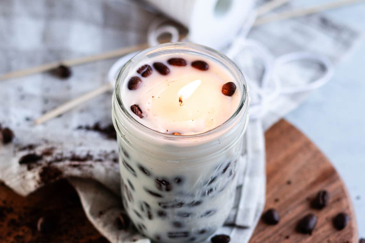 A DIY Coffee candle burning in a room with whole coffee beans spread around it.