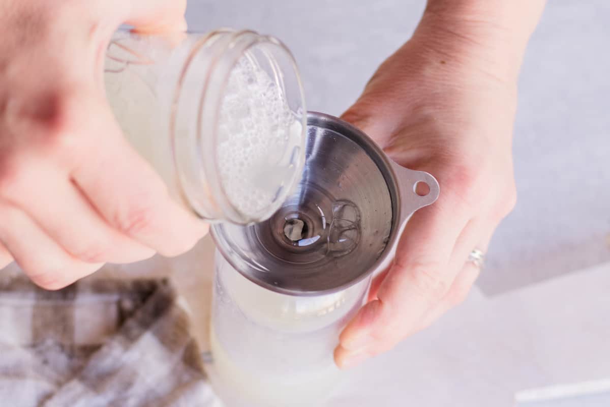 Pouring the castile soap into a soap dispenser using a funnel.