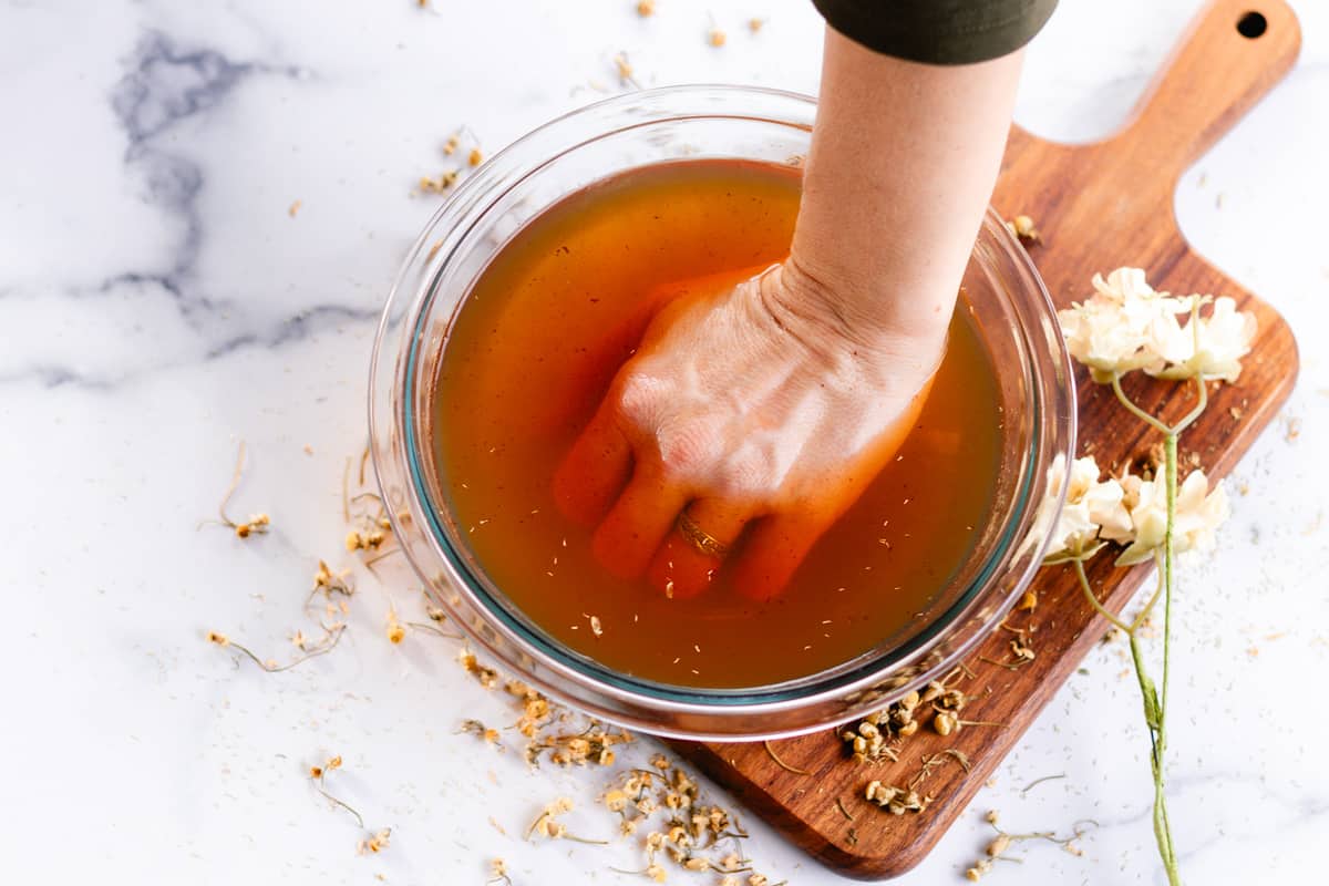 Submerging my hand into a homemade hand soak recipe on a marble table top.