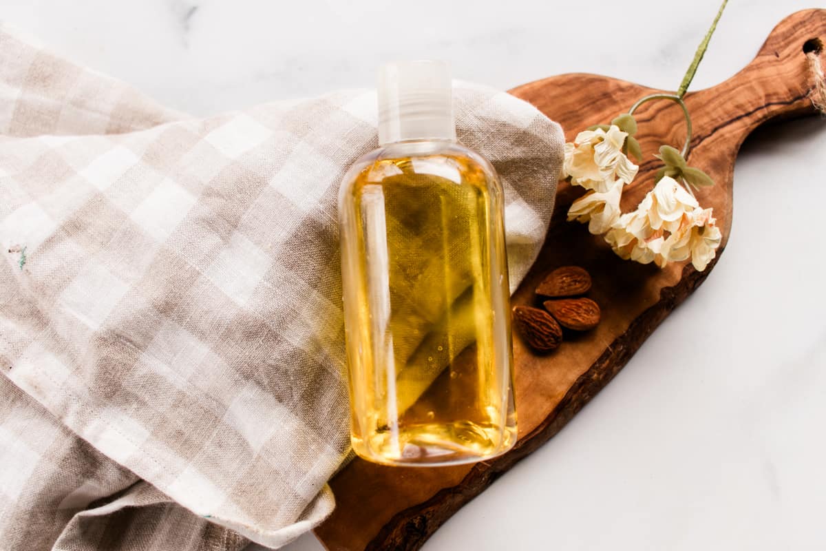 A shower oil used to moisturize the skin with a towel on a white vanity.