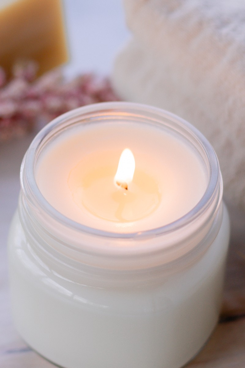 A homemade soy wax candle burning on a white table.