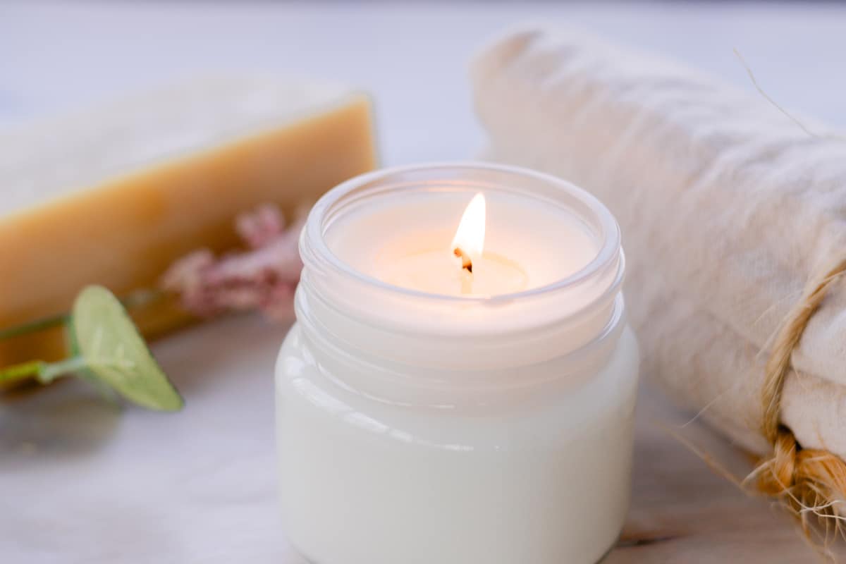 Homemade soy wax candle in a clear candle jar with a block of wax and a few flowers in the background.