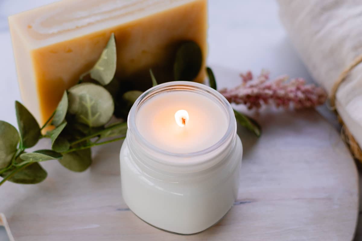 DIY soy wax candle freshly lit on a wooden top with a block of wax in the background.