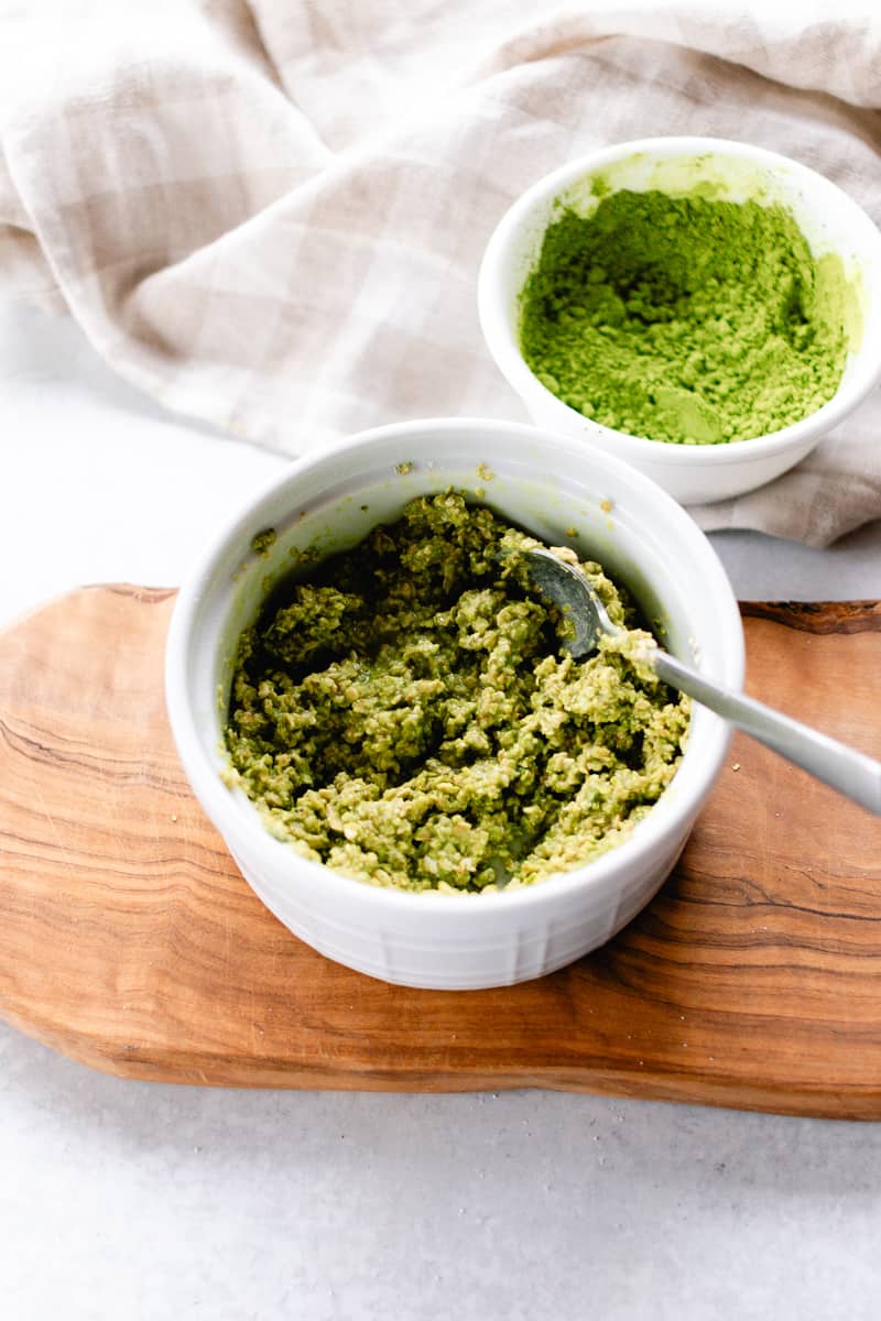 Green tea and oatmeal face mask with a bowl of green tea powder in the background.