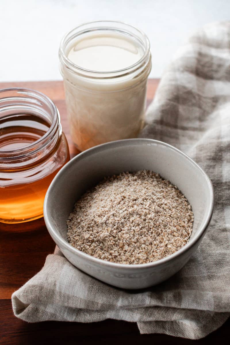 The ingredients to make an oatmeal and honey face mask in several containers.