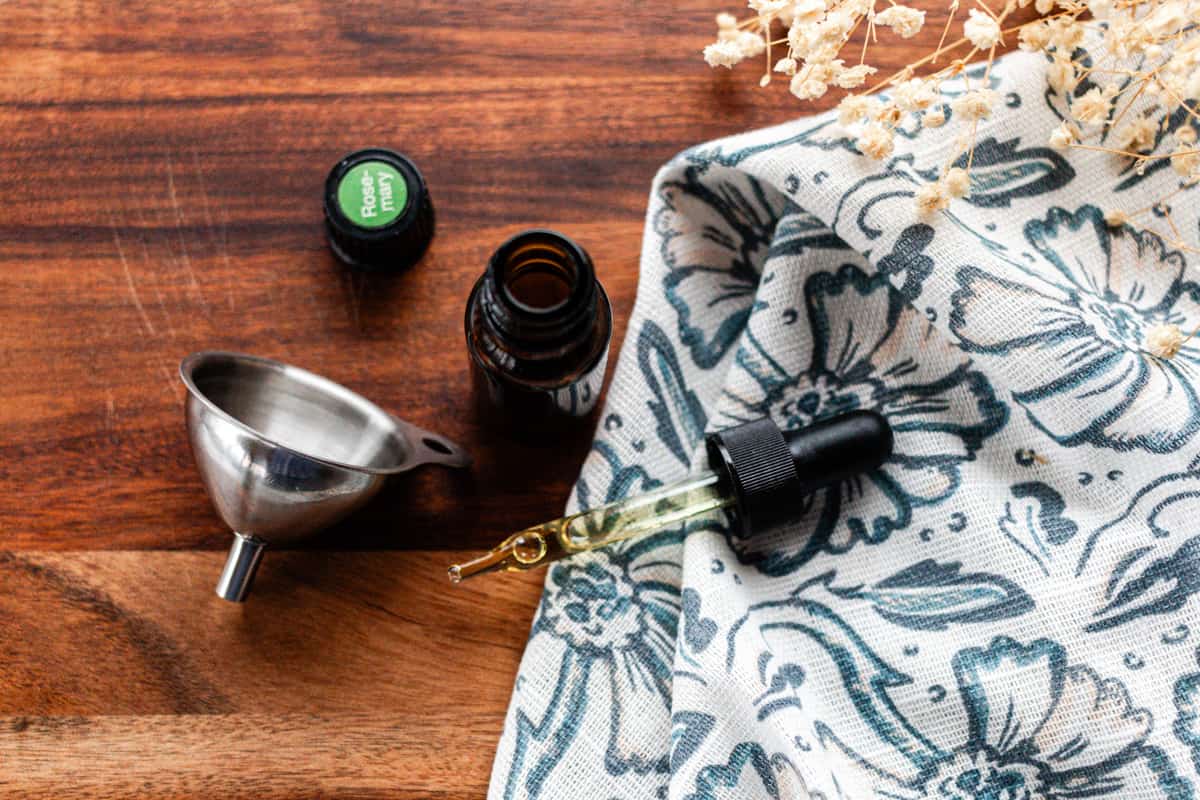 A homemade hair growth oil on a wooden table with a dropper top and a small funnel.