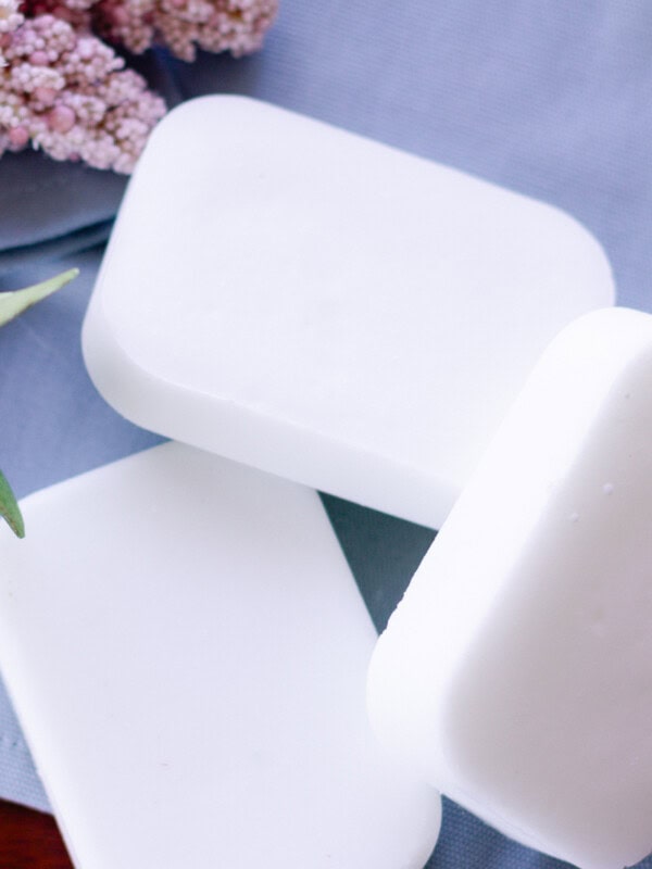 Coconut oil soap bars after they have cured sitting on a blue towel with dried flowers in the background.
