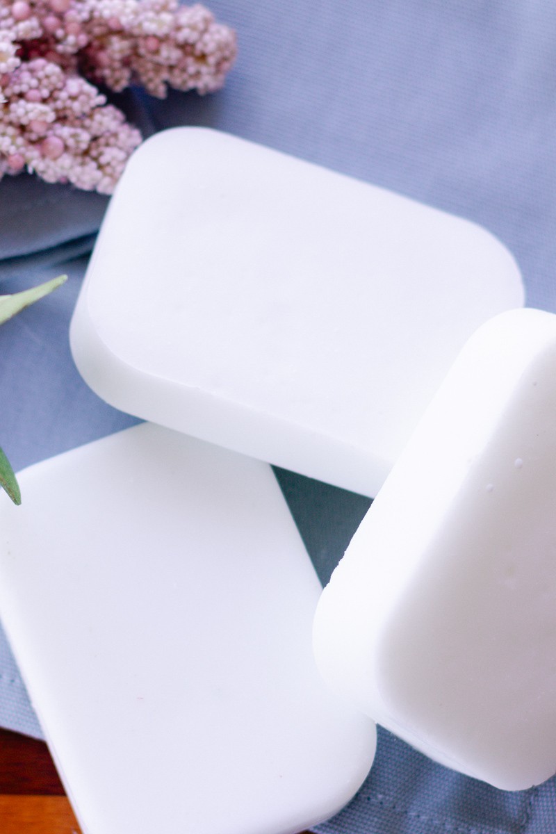 Coconut oil soap bars after they have cured sitting on a blue towel with dried flowers in the background.