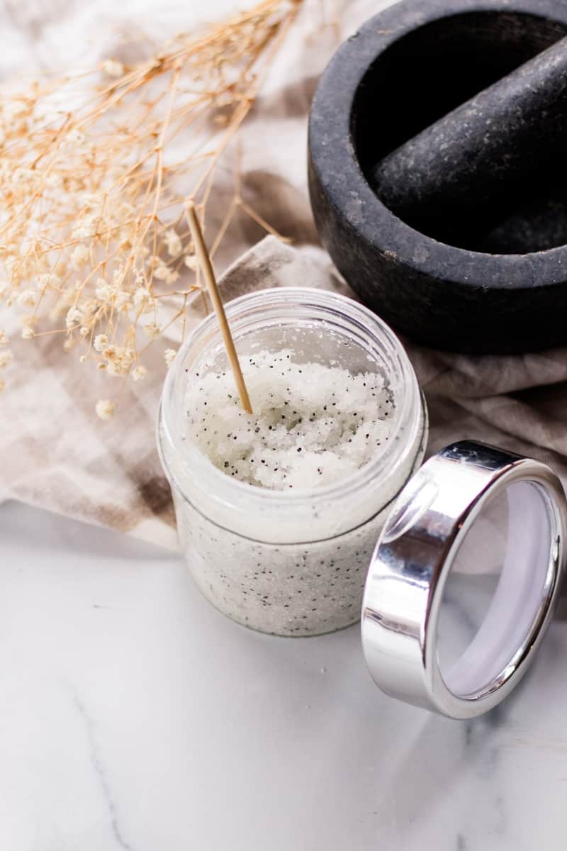 A homemade salt scrub with a wooden stirrer on a marble vanity.