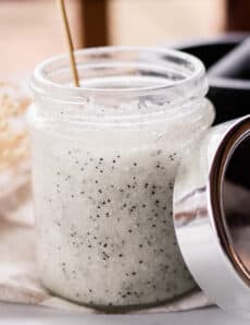 A homemade salt scrub with poppy seeds in a clear glass jar.