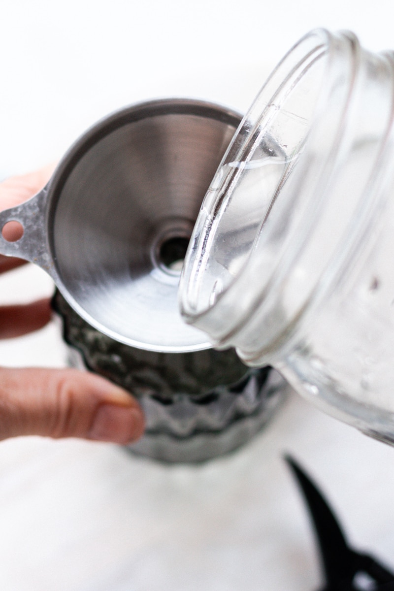 Adding the water to the room spray using a funnel.