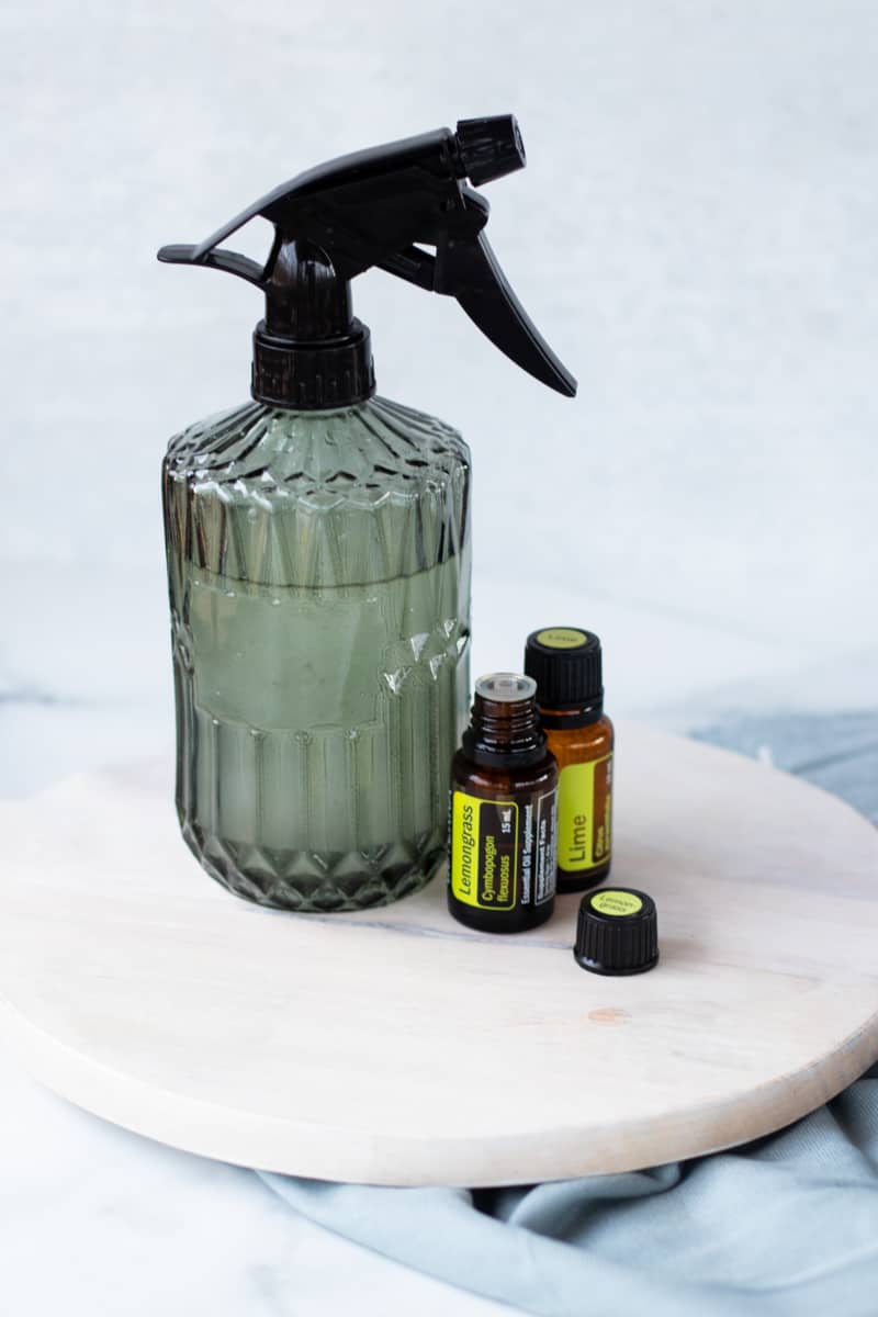 Homemade room spray in a green spray bottle with fragrance oils next to it.