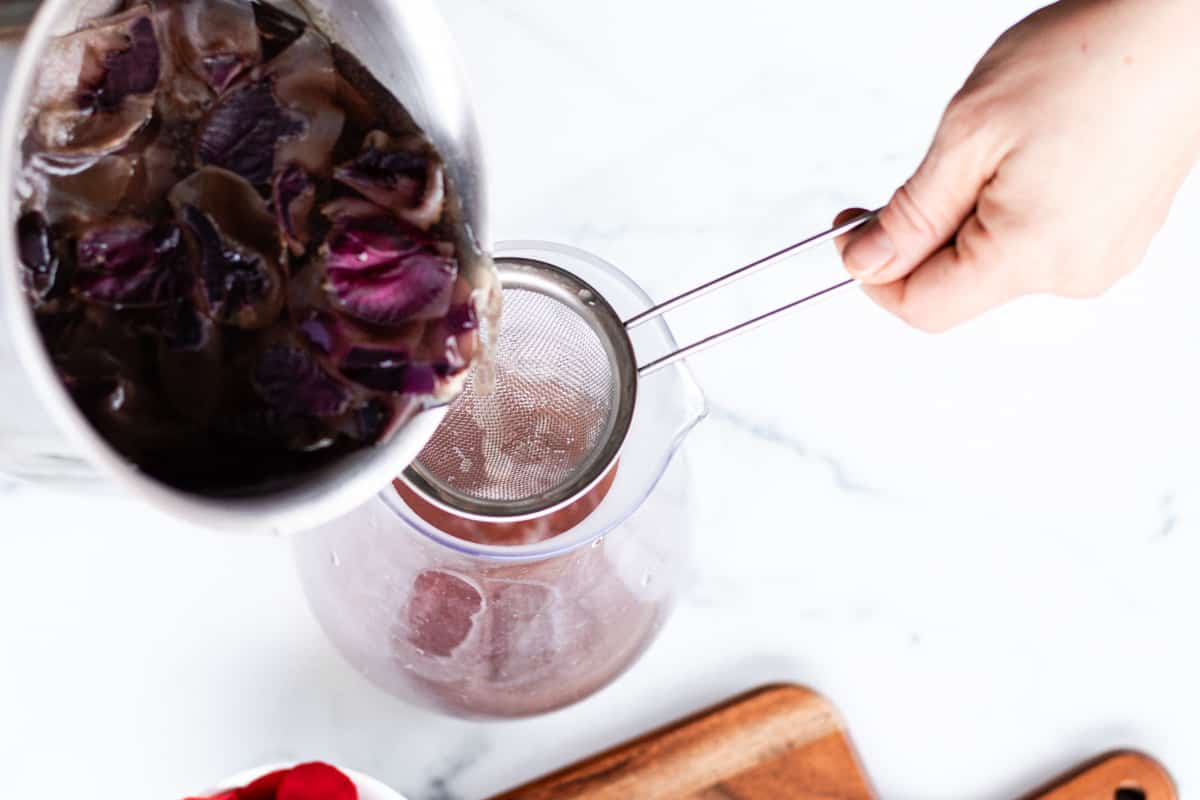 Straining the rose water out using a metal strainer.