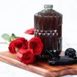 A rose water spray in a glass spray bottle with rose petals around it.