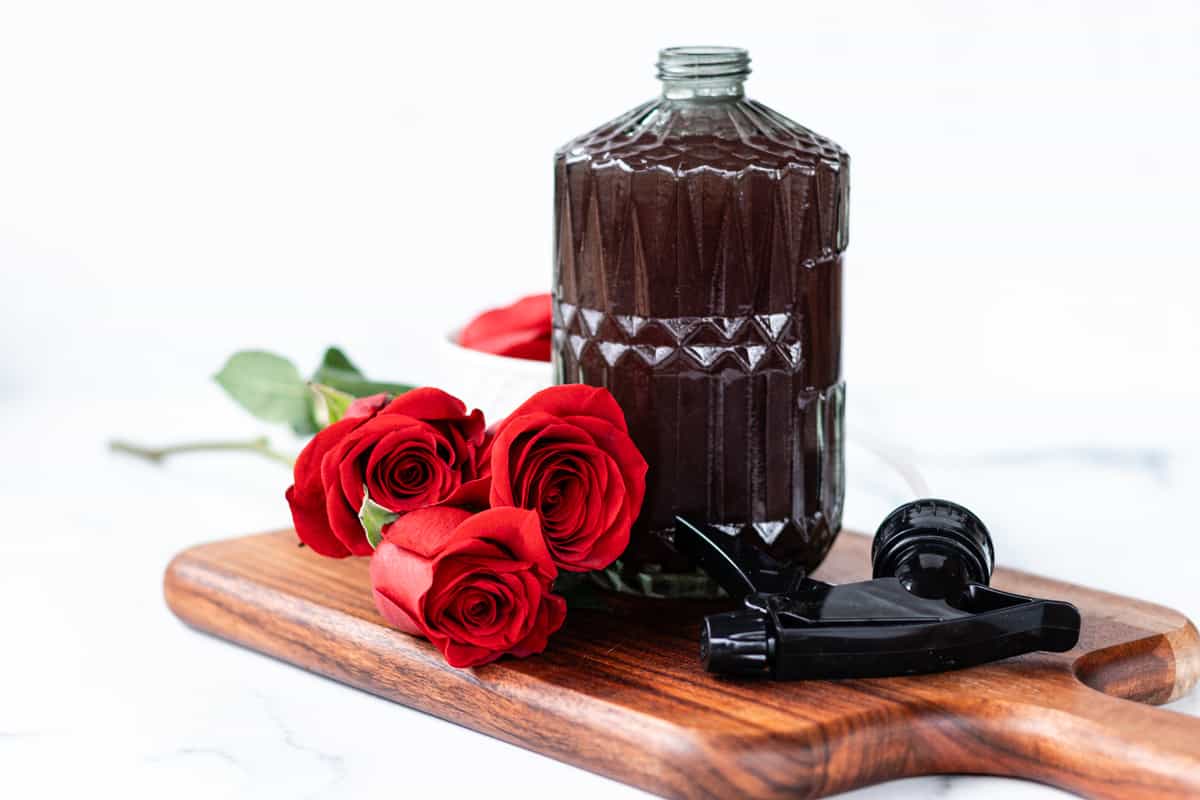 Homemade rose water in a clear container on a white marble countertop with fresh roses beside it.