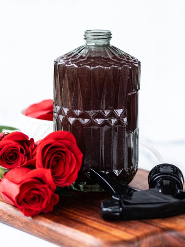Homemade rosemary water spray in a glass bottle with fresh roses next to it.