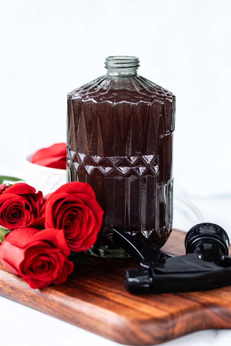 A beautiful close up shot of the rose water on a wooden board with fresh roses next to it.