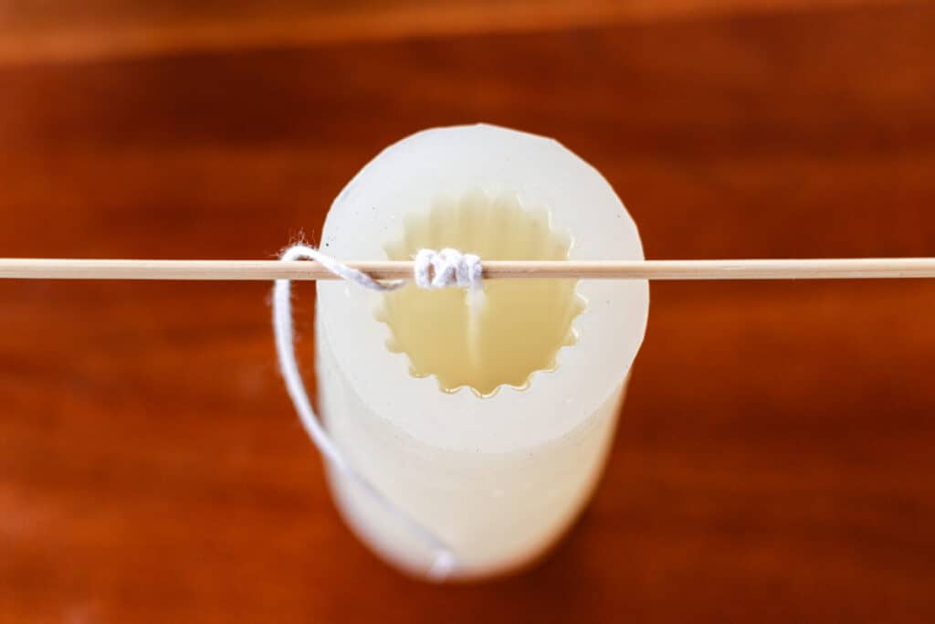 top down view of a silicone pillar candle mold filled with melted wax with the wick tied around a wooden skewer