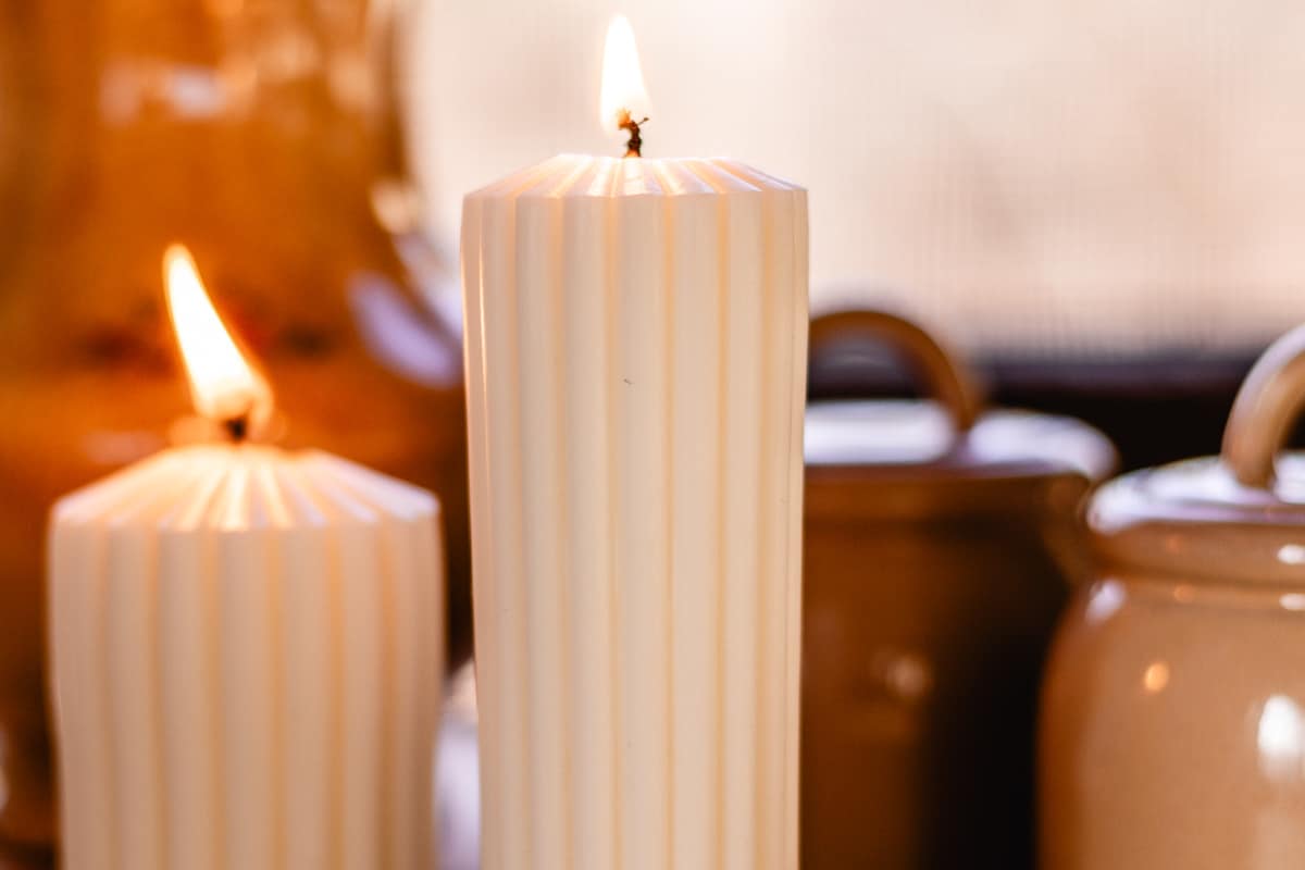 2 homemade pillar candles burning on the table with light decorations behind it. 