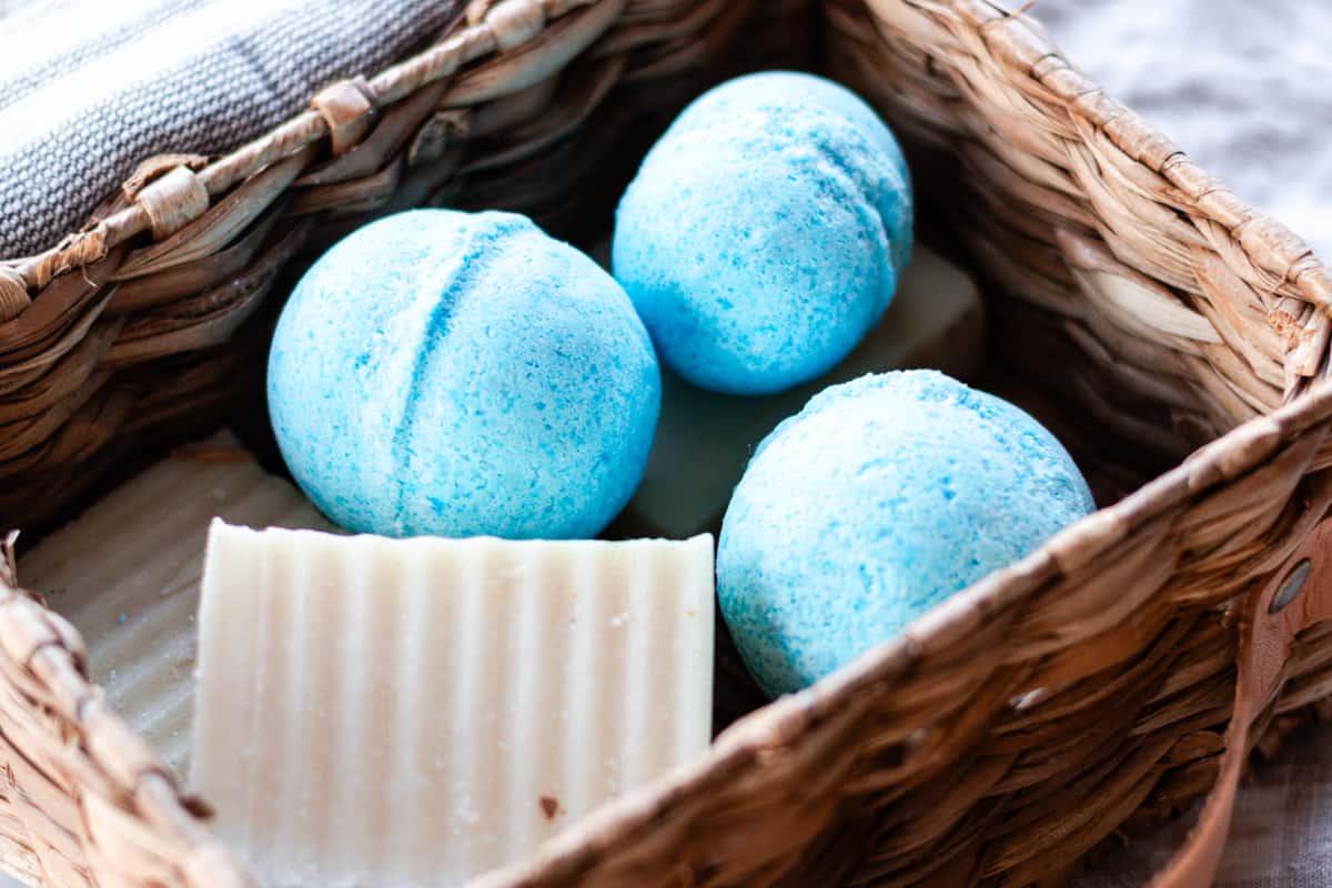 Several shower bombs in a small basket with bars of soap next to them.
