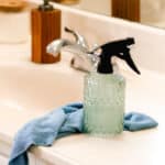 A homemade soap scum spray on a white bathroom vanity with a blue rag.