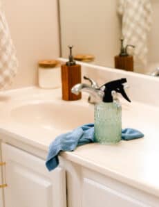 A sparkling clean bathroom with a marble vanity and a homemade soap scum remover spray with a cleaning towel on it.