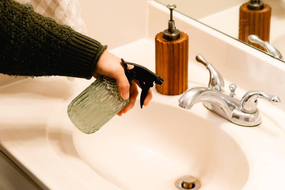 Spraying soap scum spray on a bathroom sink.