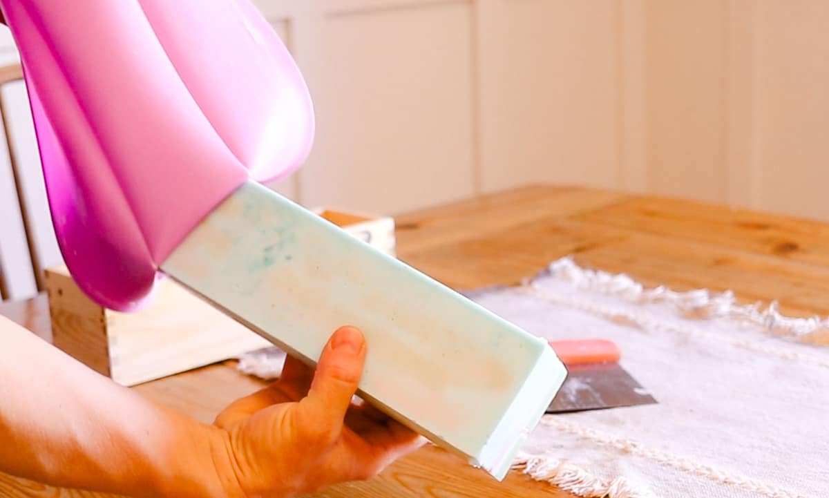 A hand removing a rectangular loaf of DIY coconut oil bar soap out of a silicone soap mold.