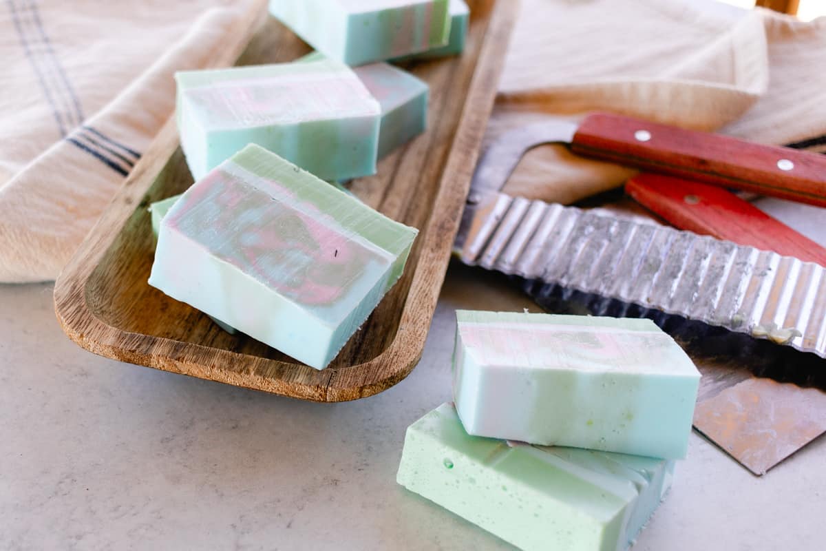 Homemade melt and pour coconut oil soap bars on a wooden tray with a wavy soap cutter.