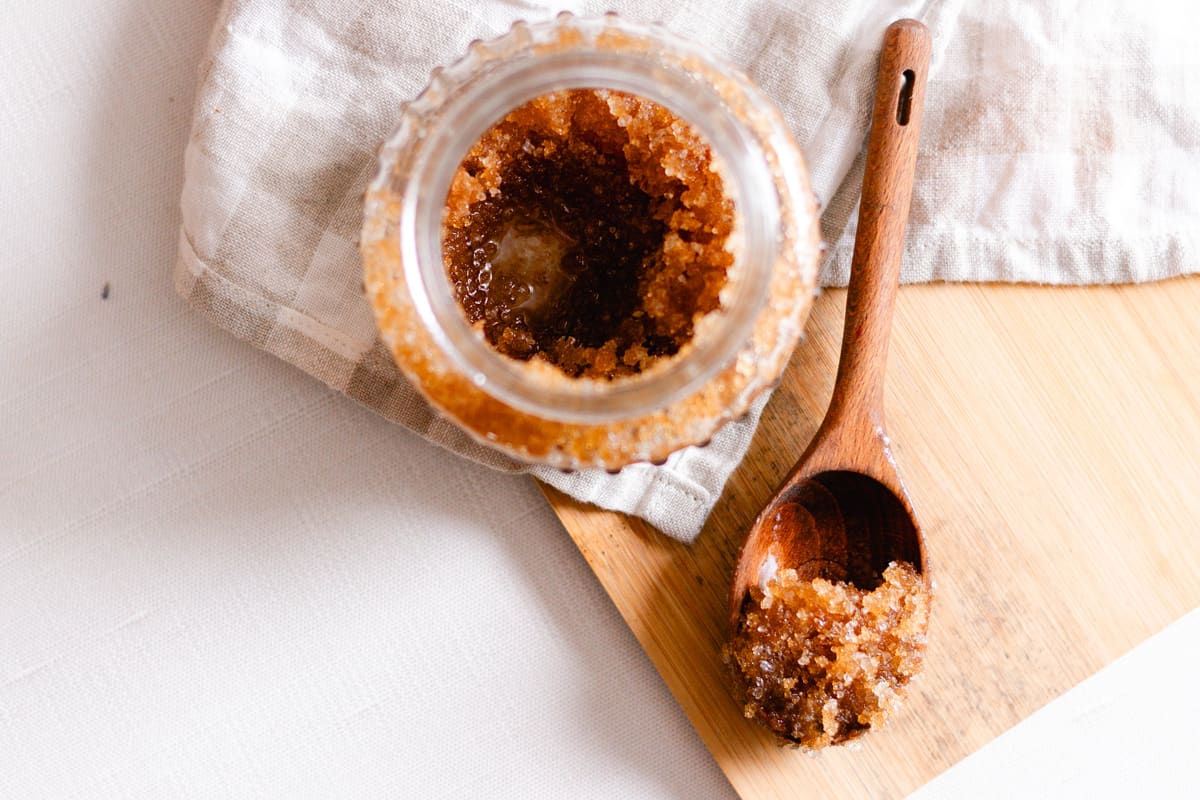 A DIY scalp scrub in a glass jar with a wooden scoop for applying.