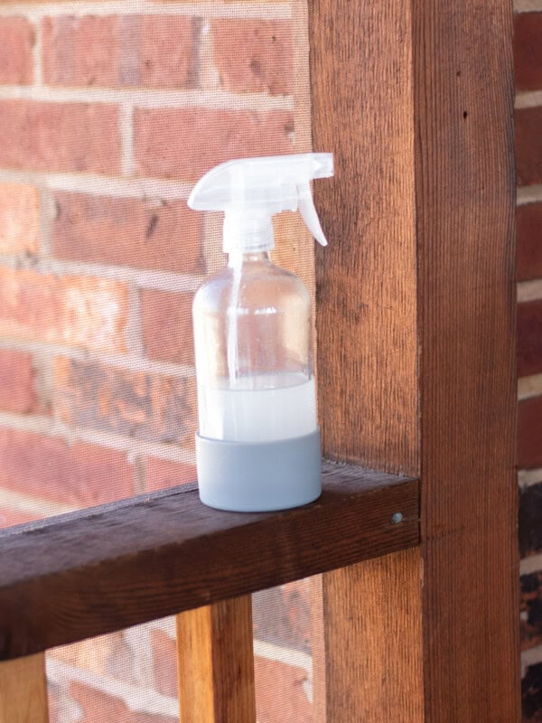 A homemade fly spray sitting on a screened in porch.