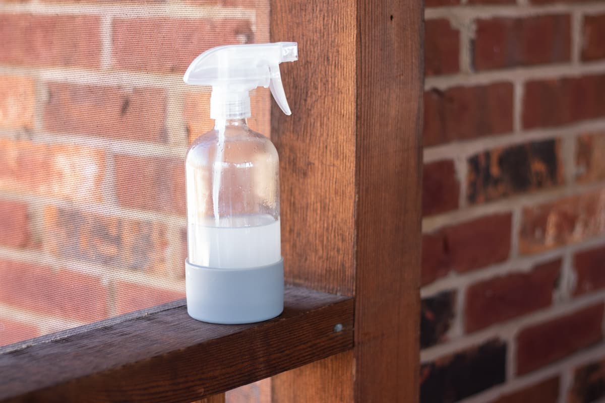 My fly repellent recipe in a clear spray bottle with a blue rubber base on a wooden railing.