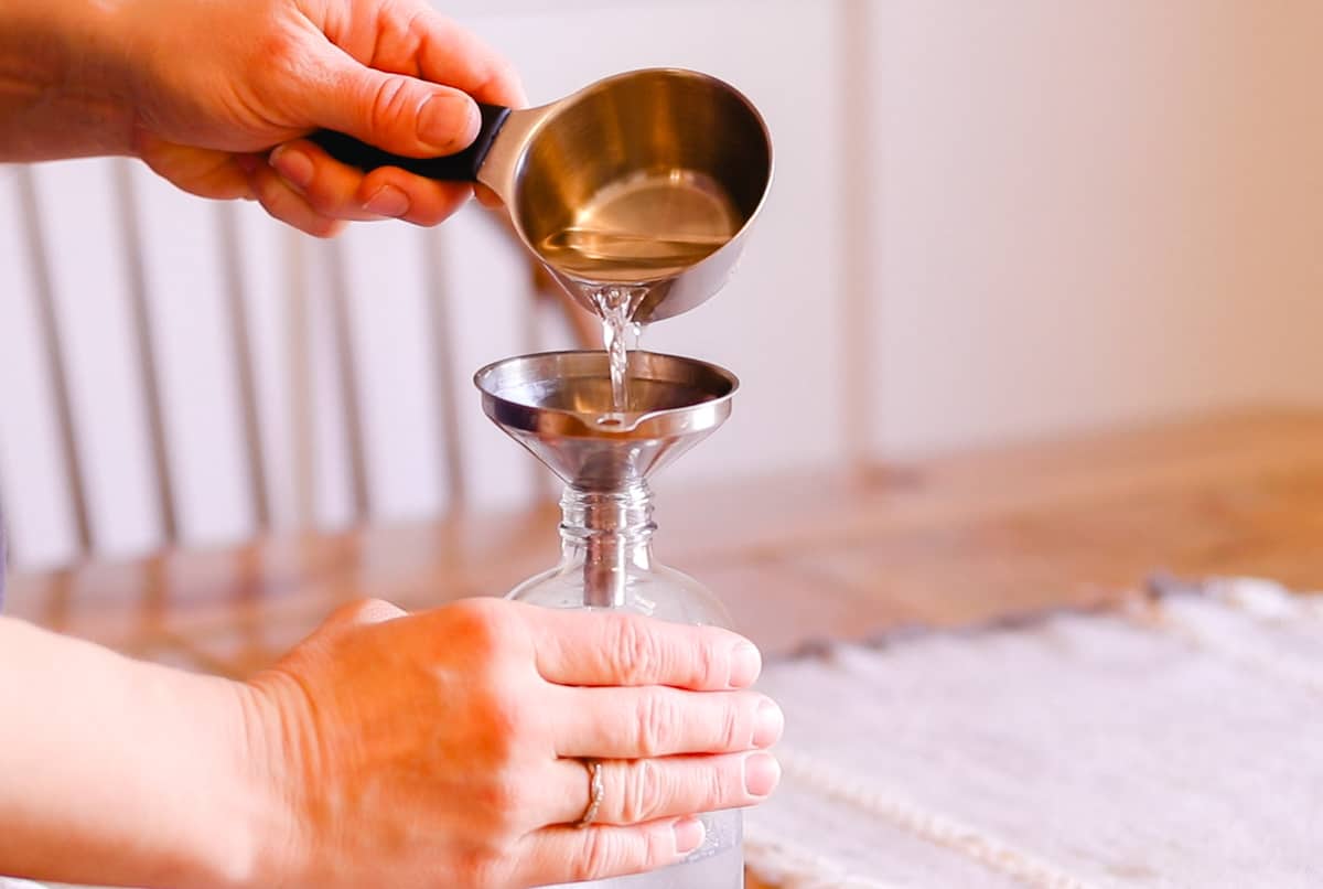 Adding rubbing alcohol and water to a spray bottle while using a funnel to prevent spills.