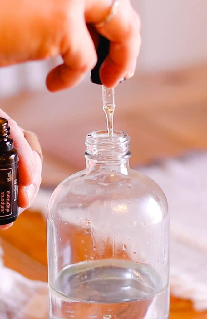 Using a dropper to measure out the correct amount of cedarwood oil to add to the spray.