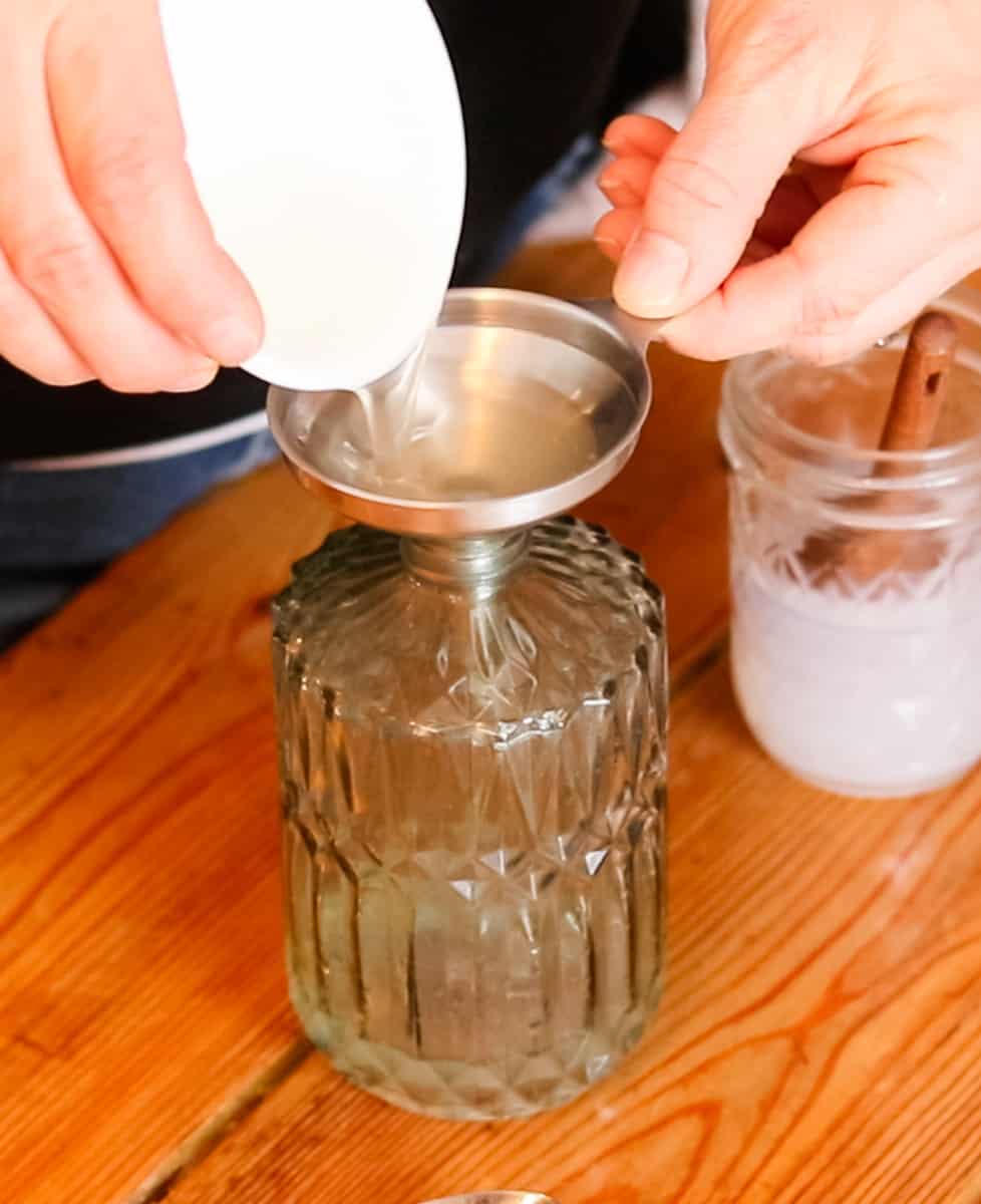 Using a metal funnel to pour homemade DIY liquid hand soap into a glass hand soap dispenser.
