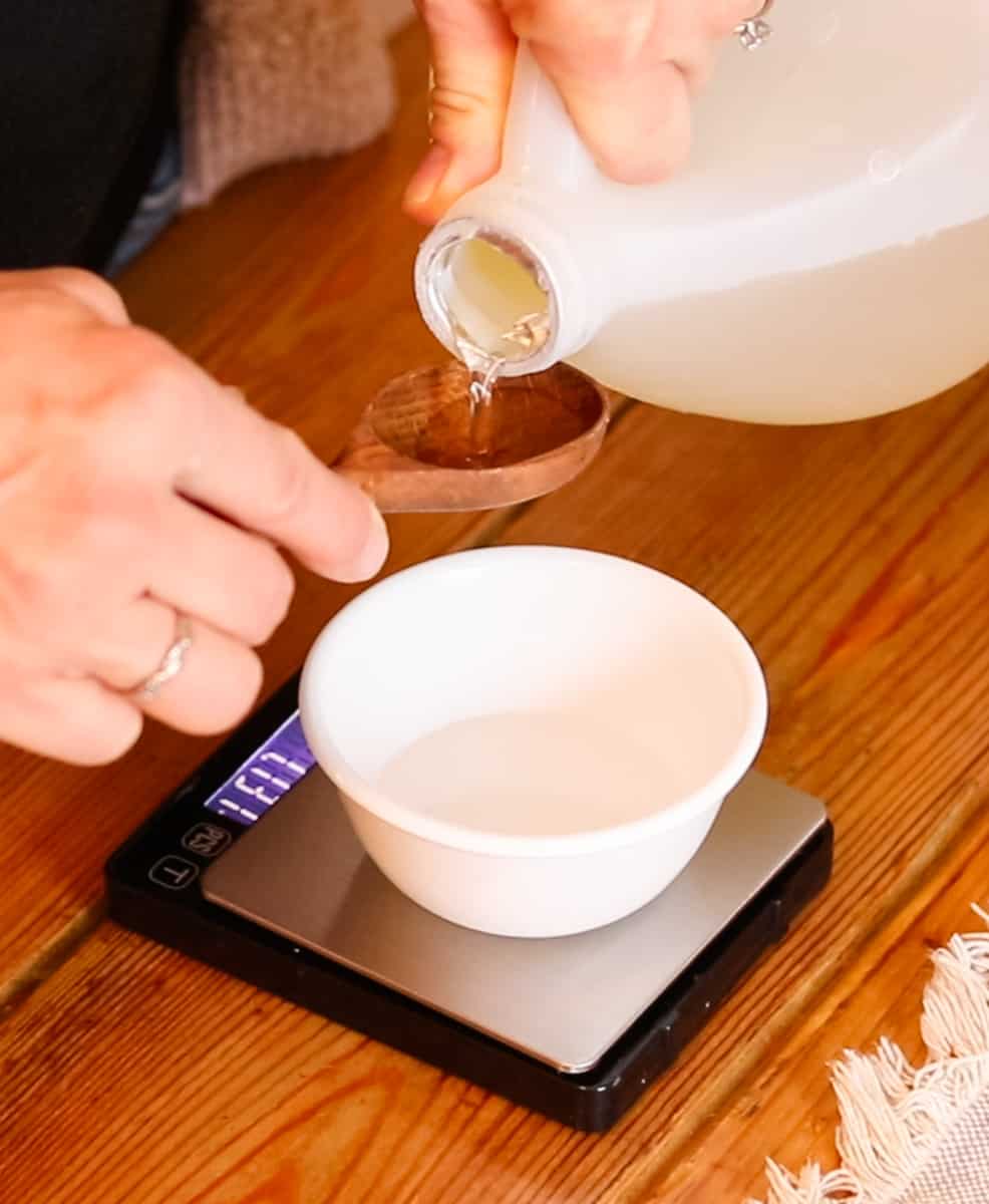Pouring castile soap into a wooden spoon held over a small bowl that is sat on top of a digital scale.