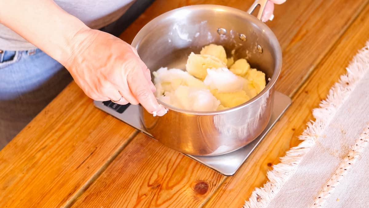 A woman melting fats and oils in a saucepan.