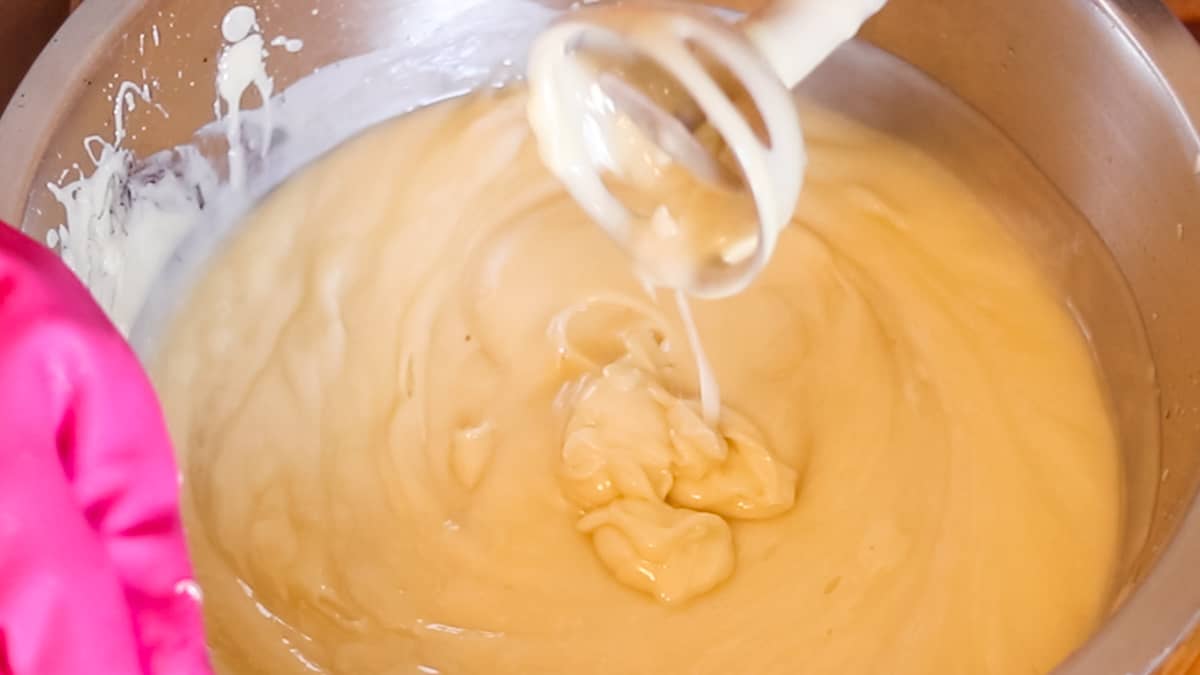 A stick blender held above soap in a large bowl filled with soap at a heavy trace.