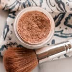 DIY bronzer in a glass jar with a bronzer brush on a white marble vanity.
