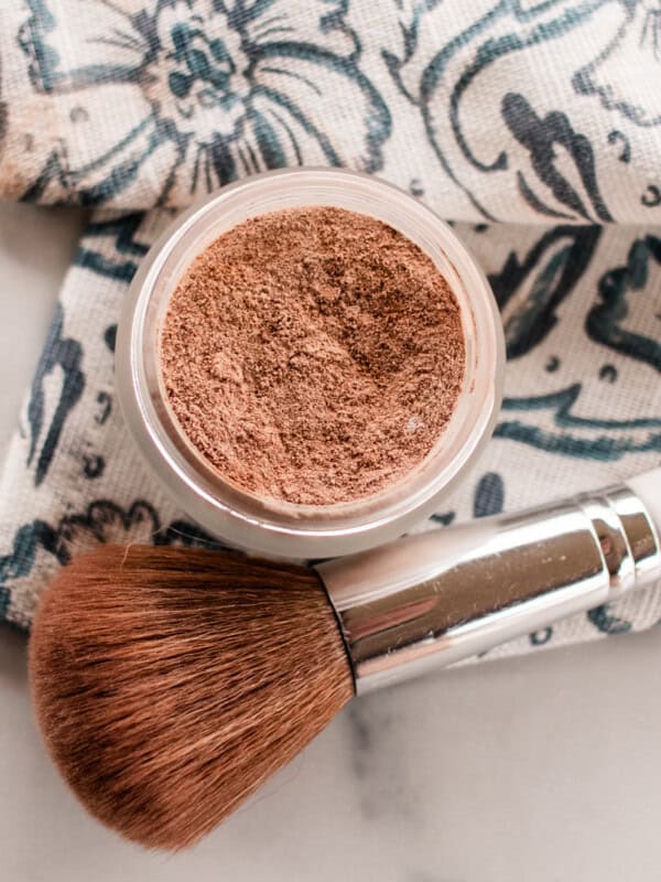DIY bronzer in a glass jar with a bronzer brush on a white marble vanity.