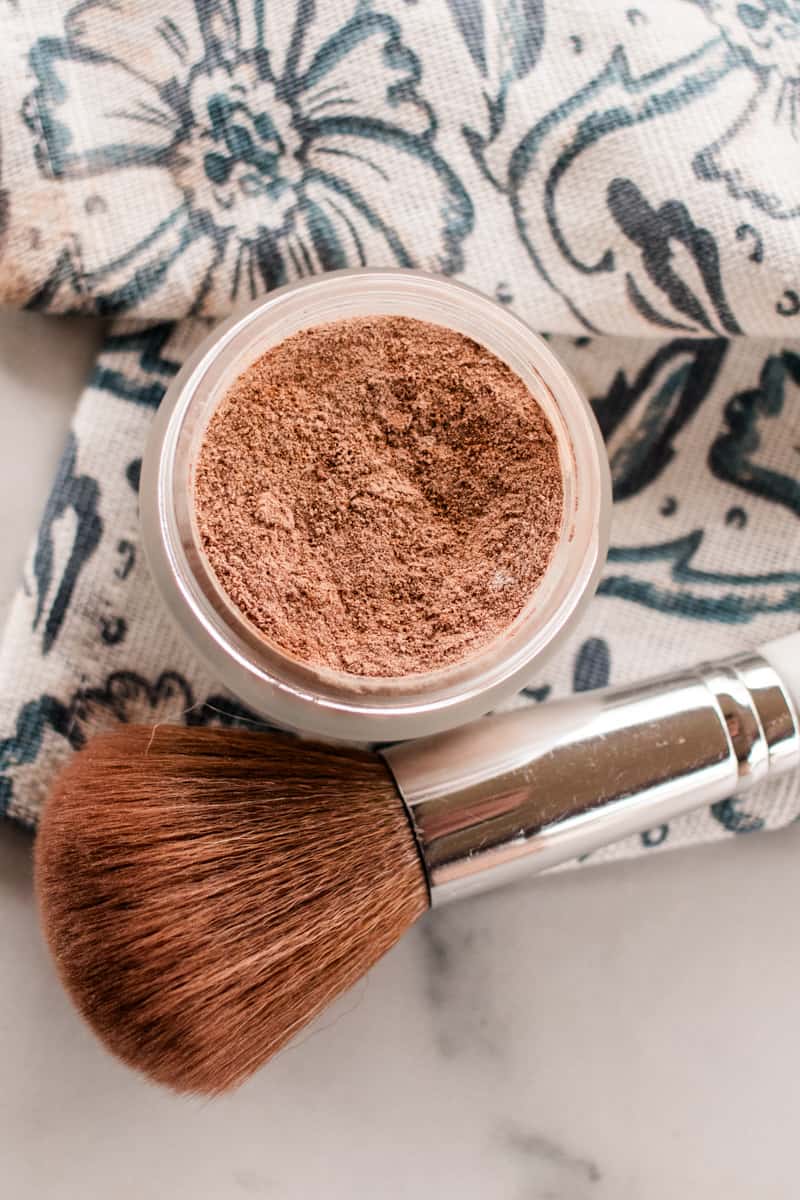 DIY bronzer in a glass jar with a bronzer brush on a white marble vanity.