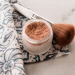 Powdered DIY bronzer in a glass jar with an applicator brush next to it.