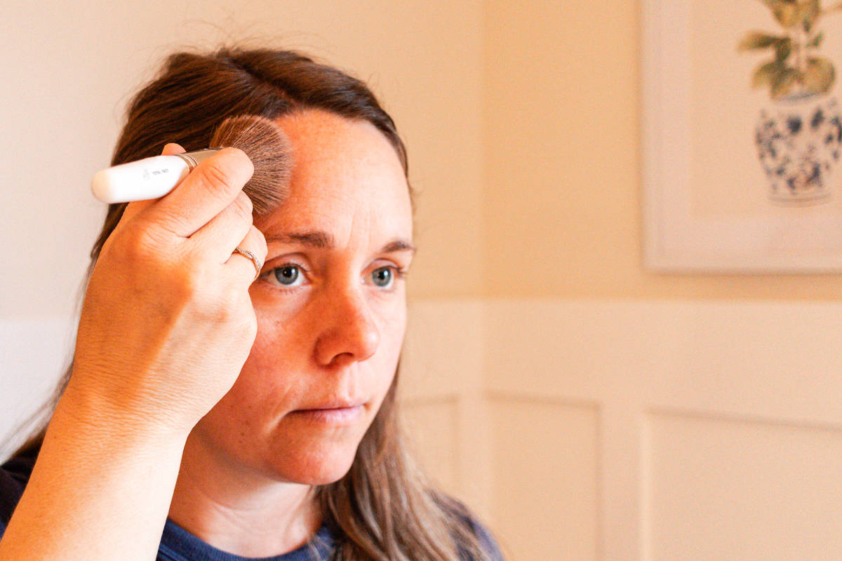 A woman using a bronzer brush to apply bronzer to her forehead.