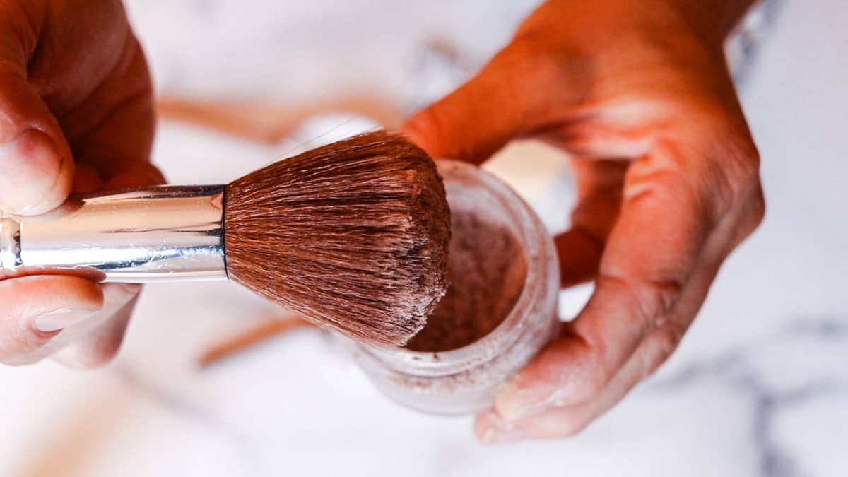 Dabbing the bronzer brush into the makeup container.