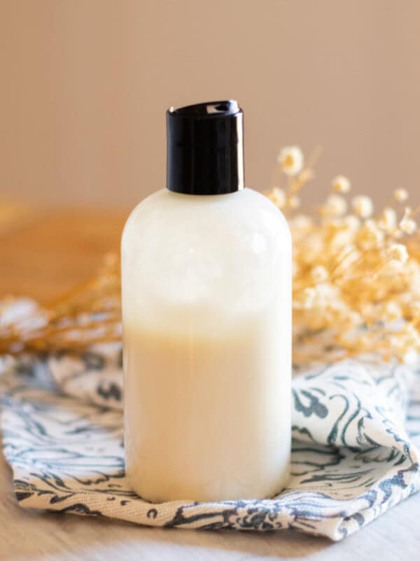 A homemade foot lotion in a plastic squeeze bottle sitting on a wooden table.